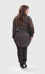 Load image into Gallery viewer, Back full body view of a woman wearing sepia alembika pants and the alembika talia russet blouse. This long sleeved blouse has a button down front, a stand collar, and a mix of different prints that are brown, black, and white.

