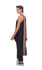 Load image into Gallery viewer, Left, back full body view of a woman wearing the alembika tekbika high low top with the alembika tekbika riding pant. The black top is sleeveless with a t-back. The back of the top has a large brown panel running down the center and comes down to just above the ankles. 

