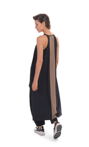 Back, full body view of a woman wearing the alembika tekbika high low top with the alembika tekbika riding pant. The black top is sleeveless with a t-back. The back of the top has a large brown panel running down the center and the hem comes down to just above the ankles.