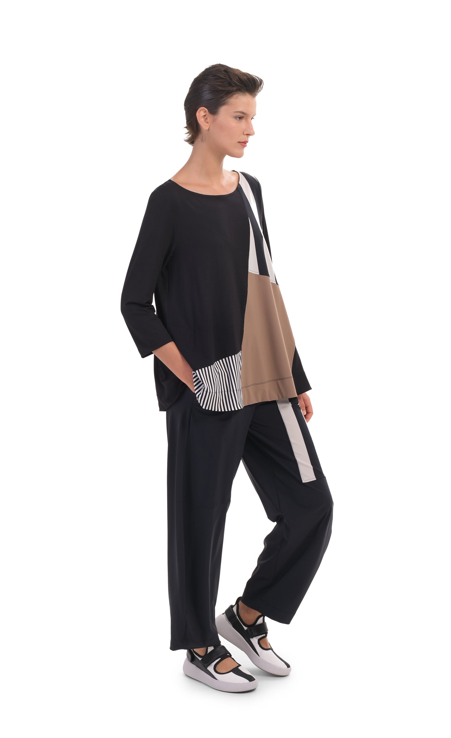 Front, left full body view of a woman wearing the alembika tekbika mixed print top. This top has 3/4 length sleeves and blocking of black and white stripes and mocha colored patches. On the bottom she is wearing a wide leg pant with a black and white striped patch.