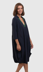 Load image into Gallery viewer, Right Side top half view of a woman wearing the alembika tekbika navy Dress. This dress sits at the knees and has a green v-neck with a collar. The dress has a bubble skirt and 3/4 length sleeves.
