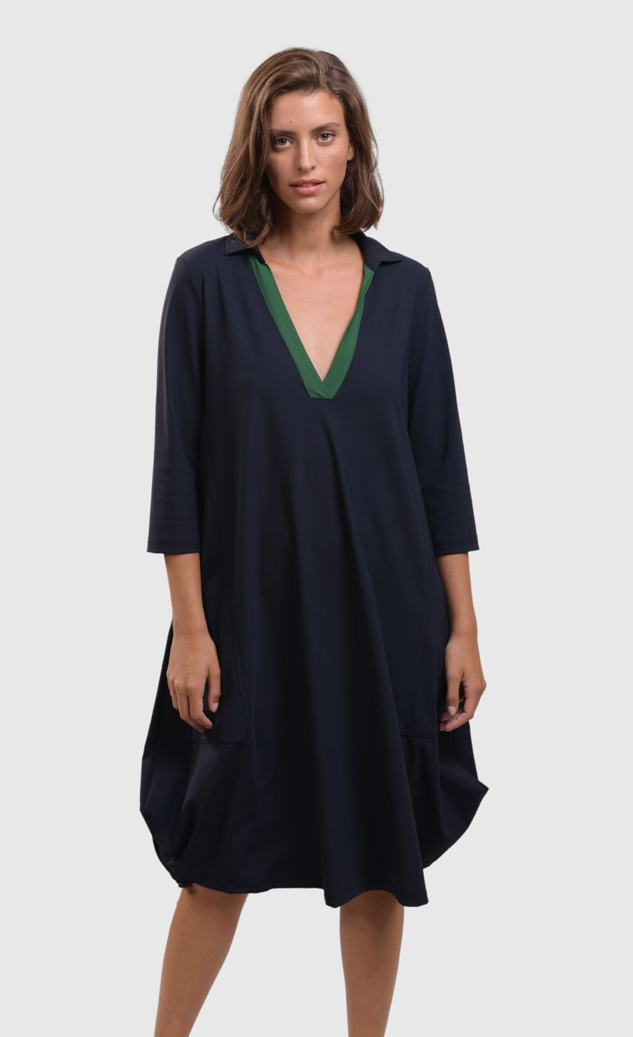 Front top half view of a woman wearing the alembika tekbika navy Dress. This dress sits at the knees and has a green v-neck with a collar. The dress has a bubble skirt and 3/4 length sleeves.