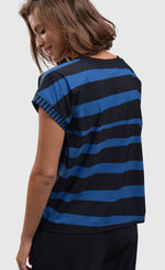 Load image into Gallery viewer, back top half view of a woman wearing the alembika tekbika ocean cap sleeve top. This top is black in the front with blue and black stripes on the back. The top has short cap sleeves and a round neck.
