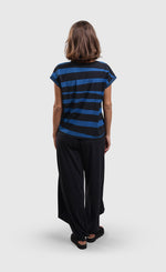 Load image into Gallery viewer, Back full body view of a woman wearing the alembika tekbika ocean cap sleeve top. This top is black in the front with blue and black stripes on the back. The top has short cap sleeves.
