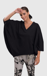 Load image into Gallery viewer, Front top half view of a woman wearing the alembika urban v neck black top and an alembika grey sketch pant. This top has drop shoulders, an oversized fit, 3/4 length dolman sleeves, and an asymmetrical hem.
