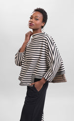 Load image into Gallery viewer, Left side top half view of a woman wearing the Alembika Urban French Terry Pants with the Alembika Urban French Terry Stripes Top. This top is white with black striping all over it. The top has an asymmetrical hem, long sleeves, a mock neck, and a boxy silhouette.
