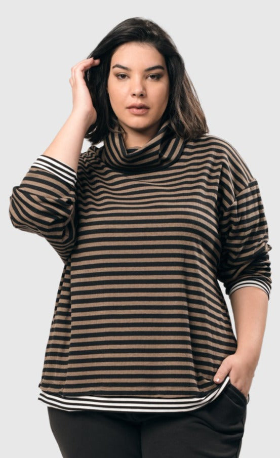 front top half view of a woman wearing the Alembika urban gateau cowlneck top in the brown and black striping. The top has a cowlneck, a relaxed fit, and contrasting black and white hems and cuffs.