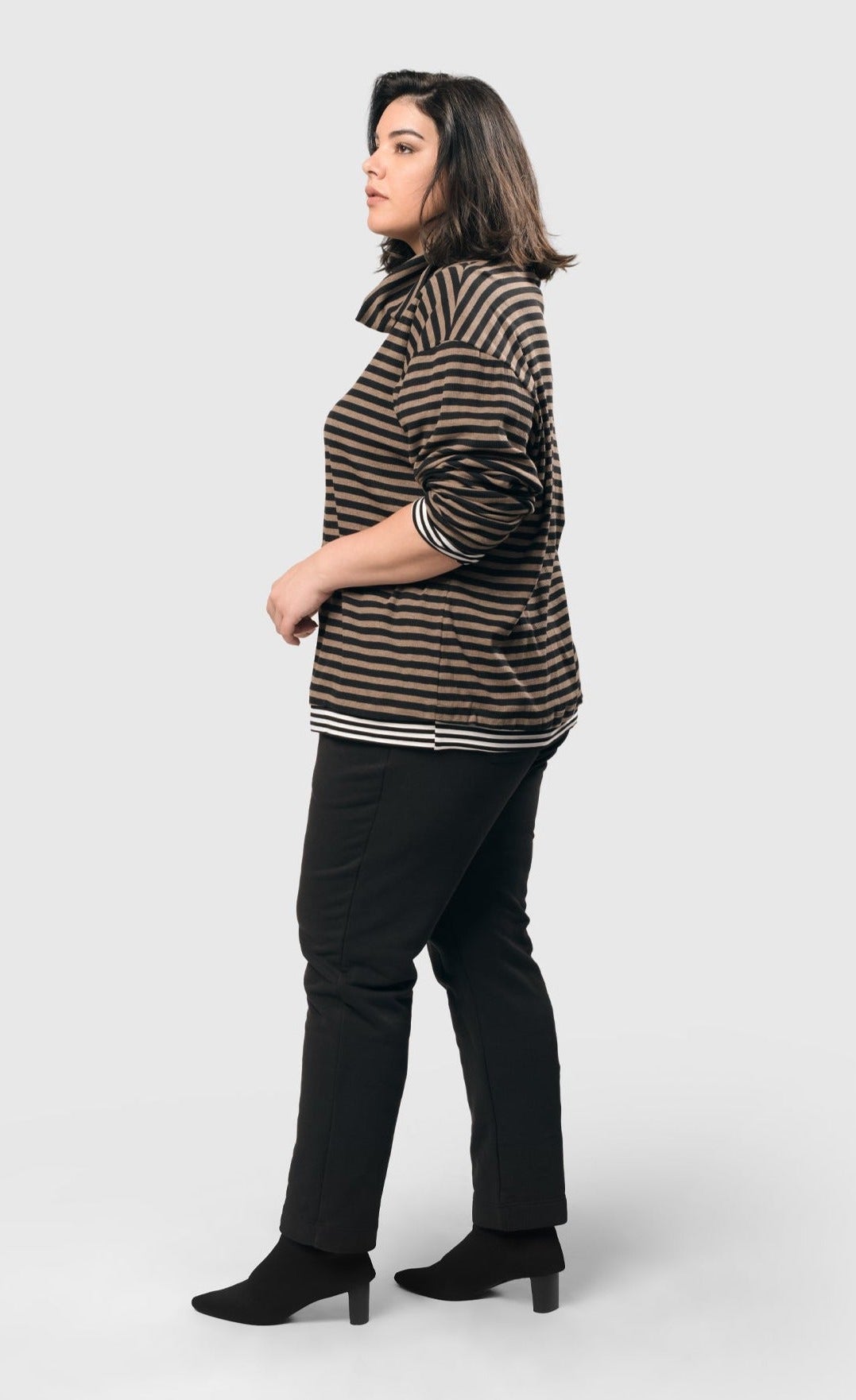 Left side top half view of a woman wearing the Alembika urban gateau cowlneck top in the brown and black striping. The top has a cowlneck, a relaxed fit, and contrasting black and white hems and cuffs.