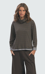 Load image into Gallery viewer, front top half view of a woman wearing the Alembika urban gateau cowlneck top in the brown and black striping. The top has a cowlneck, a relaxed fit, and contrasting black and white hems and cuffs.
