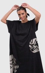 Load image into Gallery viewer, Front full body view of a woman wearing the alembika urban moon maxi dress. This dress is dark grey with two patch circles on the bottom 2/3s of the dress. These circles are white/grey with a scribble print on them. The relaxed dress sits just above the ankles and has elbow length sleeves.
