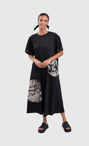 Front full body view of a woman wearing the alembika urban moon maxi dress. This dress is dark grey with two patch circles on the bottom 2/3s of the dress. These circles are white/grey with a scribble print on them. The relaxed dress sits just above the ankles and has elbow length sleeves.