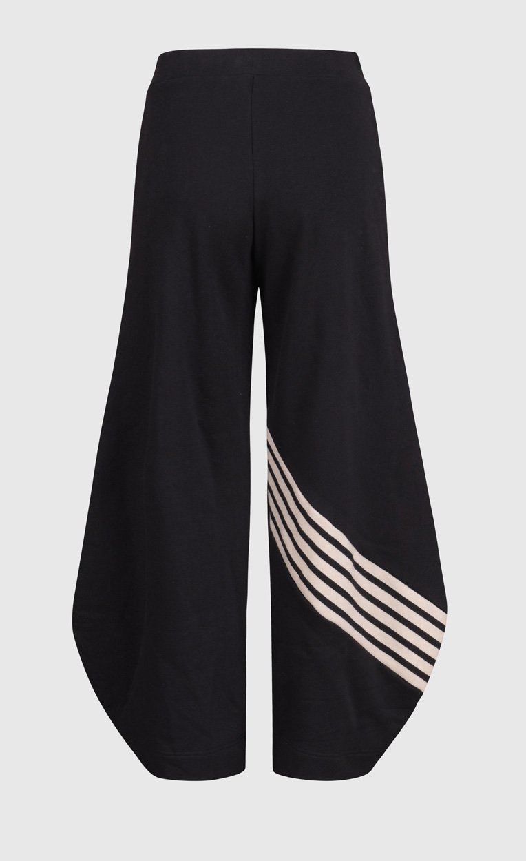 Back view of the alembike urban french terry punto pant. The wide pant is black with a black and white striped detailing on the back of the bottom of the right leg. 