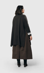 Load image into Gallery viewer, Back view of a woman wearing the alembika urban ribbon cowl neck tunic top in black. This tunic has deep side slits, a cowl neck, and long sleeves with two white stripes on the right arm.
