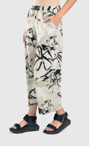 Left side bottom half view of a woman wearing the alembika urban sketch go to pant. This pant is grey white with black and dark grey scribbles all over it. The pant has two side pockets, a cropped cut, and wide legs.