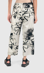 Load image into Gallery viewer, Back bottom half view of a woman wearing the alembika urban sketch go to pant. This pant is grey white with black and dark grey scribbles all over it. The pant has a cropped cut, and wide legs.
