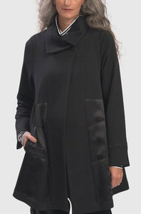 Front top half  view of a woman wearing the alembika urban sleek satin trim jacket in black. This jacket has a single button closure and satin panels on the side. 