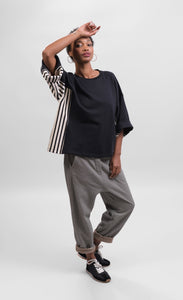 Front full body view of a woman wearing striped pants and the alembika urban black/striped panel top. This top is black with wide folded sleeves that sit at the elbows. The top has black and white striped paneling on the sides and under the arms.