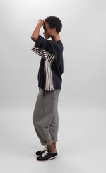 Load image into Gallery viewer, Left side full body view of a woman wearing striped pants and the alembika urban black/striped panel top. This top is black with wide folded sleeves that sit at the elbows. The top has black and white striped paneling on the sides and under the arms.

