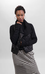 Load image into Gallery viewer, Front top half view of a woman wearing a black and white striped skirt and the alembika urban puffer vest in black. This vest has a ribbed collar and a front single button.
