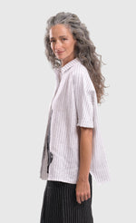 Load image into Gallery viewer, Left side top half view of a woman wearing the alembika striped white cactus shirt. This white shirt has black pinstripes, a button down front, short sleeves, a collar, and a black cactus print on the bottom of the front.
