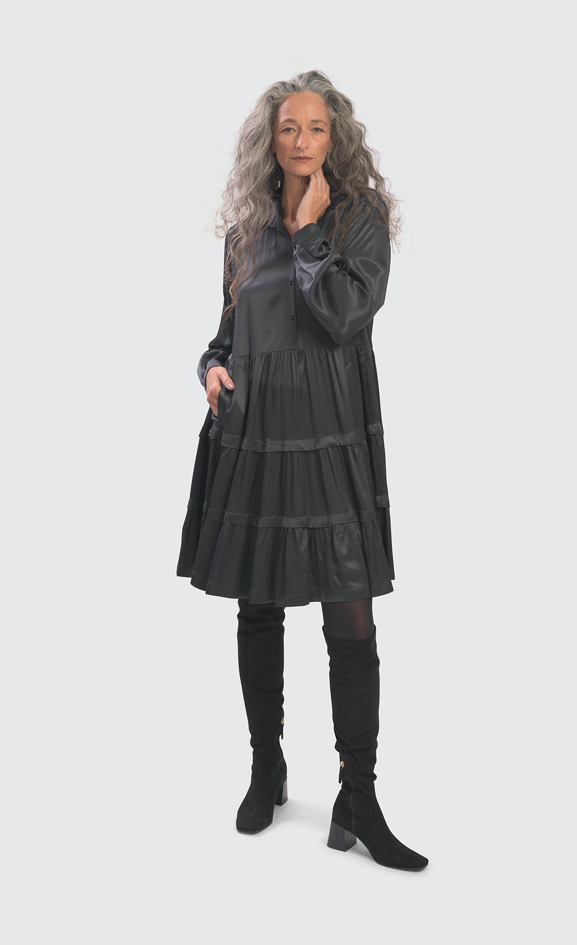 Front full body view of a woman wearing the alembika urban satin babydoll dress. This dress is steel colored and shiny. It has a button down front, long sleeves, and a tiered skirt.