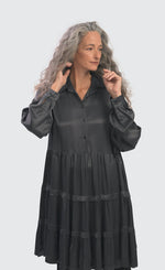 Load image into Gallery viewer, Front top half view of a woman wearing the alembika urban satin babydoll dress. This dress is steel colored and shiny. It has a button down front, long sleeves, and a tiered skirt.
