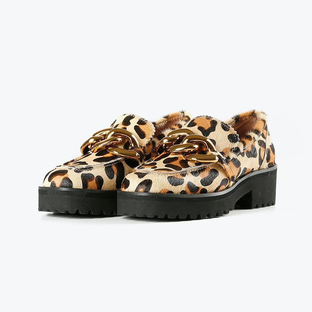 front view of a pair of the all black footwear chunky lugg lady shoe. This lugg sole shoe has leopard printed calf hair all over the outer and decorative gold chain hardware in the front