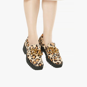 front view of a pair of the all black footwear chunky lugg lady shoe. This lugg sole shoe has leopard printed calf hair all over the outer and decorative gold chain hardware in the front