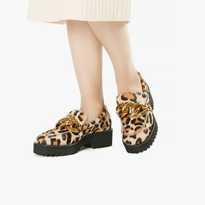 Front view of a pair of the all black footwear chunky lugg lady shoe. This lugg sole shoe has leopard printed calf hair all over the outer and decorative gold chain hardware in the front