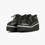 Load image into Gallery viewer, Front view of a pair of the all black footwear kiltie ox flatform. This shoe is black with a black platform sole and a lace up front. The sole and leather upper are separated by white piping around the shoe.
