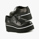 Load image into Gallery viewer, Outer and inner side view of a pair of the all black footwear kiltie ox flatform. This shoe is black with a black platform sole and a lace up front. The sole and leather upper are separated by white piping around the shoe.
