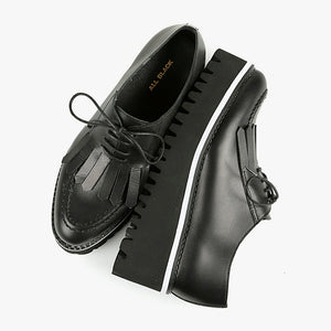 birdseye view of a pair of the all black footwear kiltie ox flatform. This shoe is black with a black platform sole and a lace up front. The sole and leather upper are separated by white piping around the shoe.
