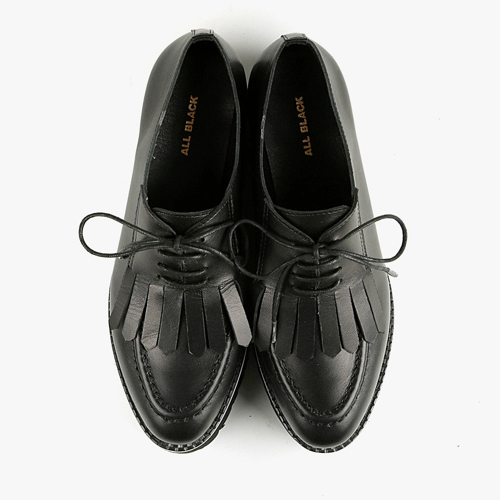 Birdseye view of the all black footwear kiltie ox flatform. This shoe is black with a black platform sole and a lace up front. The sole and leather upper are separated by white piping around the shoe.