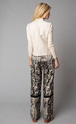 Load image into Gallery viewer, Back, full body view of a woman wearing a beige jacket with fitted sleeves. On the bottom-half, she is wearing the Lola &amp; Sophie Animal Border Print Pull-On Pant. These pants feature a smudge print and a snake print separated by a back stripe that runs horizontally across the leg near the knee. These relaxed, straight pants have a side slit that goes up to the knee.
