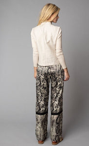 Back, full body view of a woman wearing a beige jacket with fitted sleeves. On the bottom-half, she is wearing the Lola & Sophie Animal Border Print Pull-On Pant. These pants feature a smudge print and a snake print separated by a back stripe that runs horizontally across the leg near the knee. These relaxed, straight pants have a side slit that goes up to the knee.