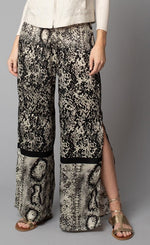 Load image into Gallery viewer, Front, bottom half view of a woman wearing the Lola &amp; Sophie Animal Border Print Pull-On Pant. These pants feature a smudge print and a snake print separated by a back stripe that runs horizontally across the leg near the knee. These relaxed, straight pants have a side slit that goes up to the knee.
