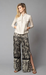 Front, full body view of a woman with her hands in the front pockets of the beige button up jacket she is wearing. On the bottom-half, she is wearing the Lola & Sophie Animal Border Print Pull-On Pant. These pants feature a smudge print and a snake print separated by a back stripe that runs horizontally across the leg near the knee. These relaxed, straight pants have a side slit that goes up to the knee.