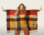 Load image into Gallery viewer, Front top half view of a woman wearing the desigual plaid poncho with brown pants. This poncho is brown, red, orange, and green plaid. It has a hood and a fringed hem.

