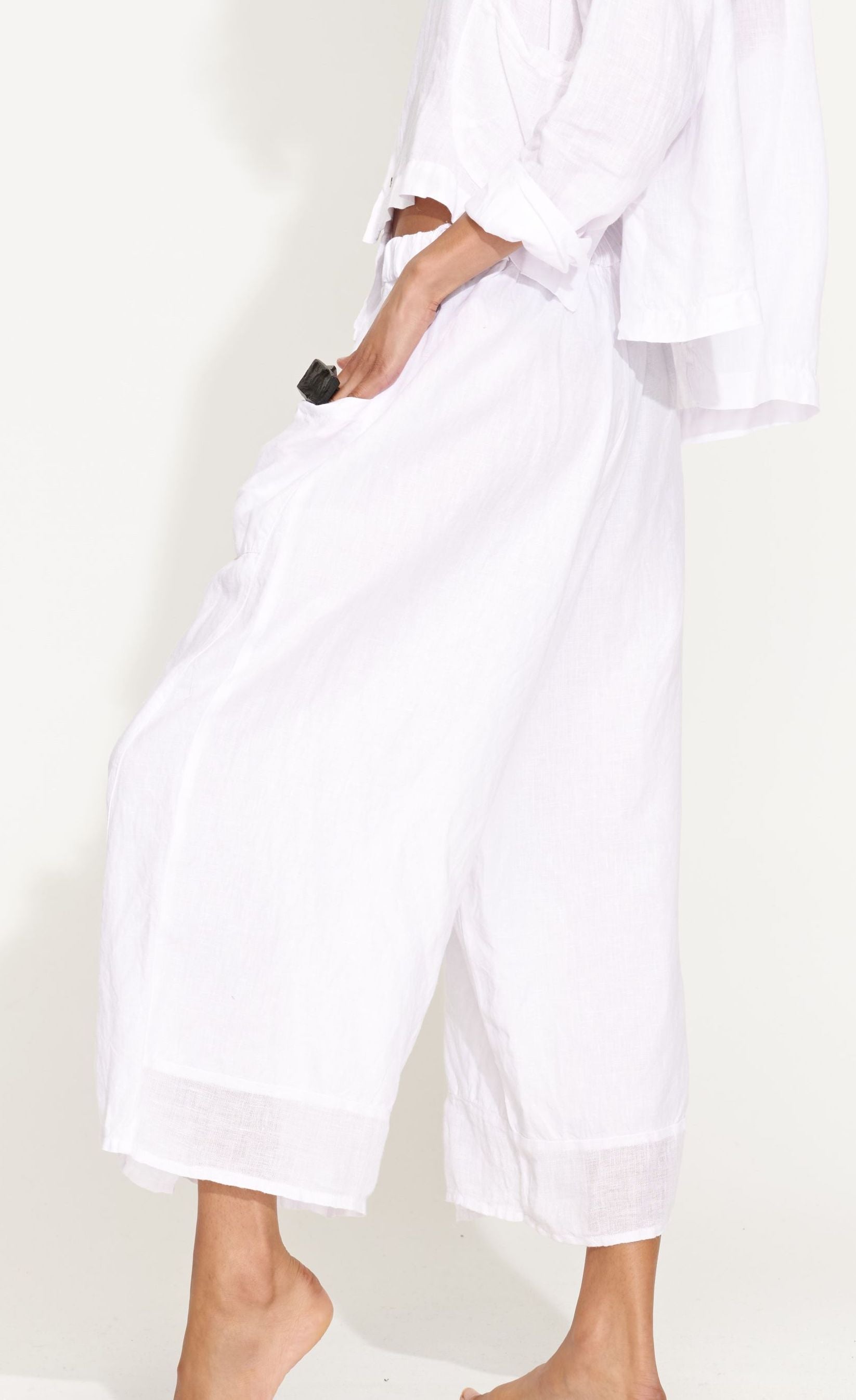Left side bottom half view of a woman wearing the banana blue solid white pant. This pant has two front pockets and a wide cropped cut.