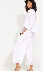Load image into Gallery viewer, Left side full body view of a woman wearing the banana blue solid white pant with a white shirt. This pant has two front pockets and a wide cropped cut.
