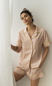 Front view of a woman wearing the coffee shoppe banana pj set. This set is pink with a banana print all over it. . The top is a button down short sleeve and the bottom are shorts.