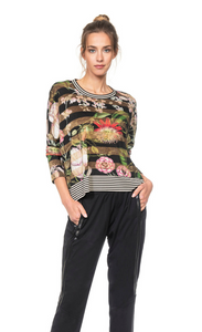 Front top half view of a woman wearing black joggers and the Beate Heymann Floral Striped Top. This top is striped black and gold with flowers on top of it. The neck and the hem have black and white striped trim. The top also has long sleeves.