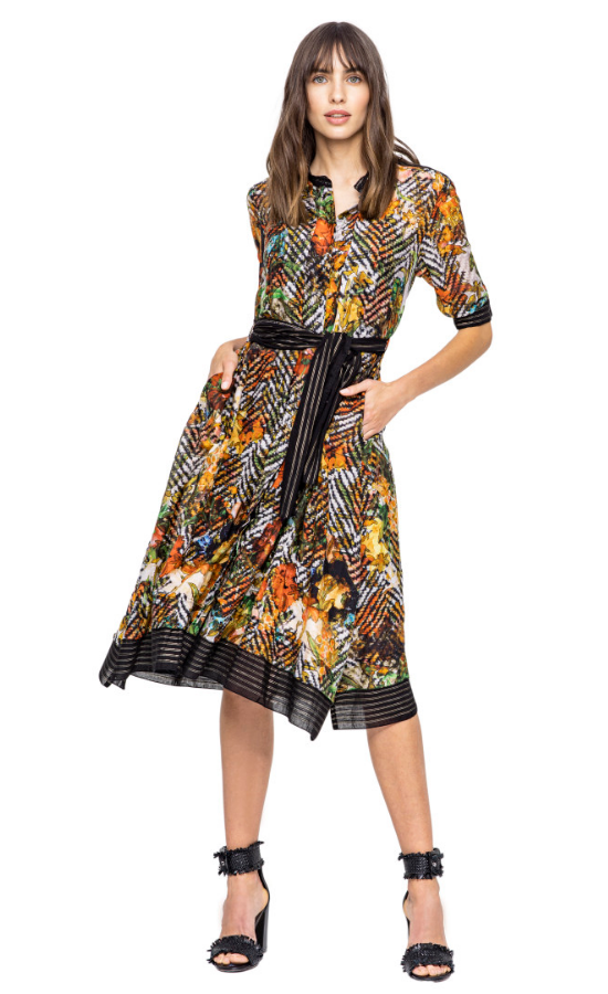 front full body view of a woman wearing closed the beate heymann colorful blouse dress. This dress has a button down front, elbow length sleeves and sits at the knees. The dress has a multicolor floral print with black chevron mixed in. The hem has black striped detailing. The dress also has a black striped tie belt at the waist.