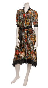 front full body view of a mannequin wearing closed the beate heymann colorful blouse dress. This dress has a button down front, elbow length sleeves and sits at the knees. The dress has a multicolor floral print with black chevron mixed in. The hem has black striped detailing. The dress also has a black striped tie belt at the waist.