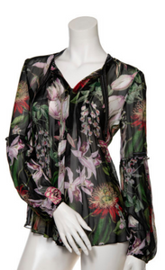 Front view of a mannequin wearing the beate heymann floralis blouse. This top is black with a floral print and transparent. It has long sleeves and a v-neck.
