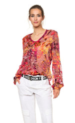 Load image into Gallery viewer, Front top half view of a woman wearing the beate heymann fuchsia firewall blouse. This blouse has a mixed red, pink, and orange print and is see through. The top also has long sleeves, a front inverted pleat, and a round neck.
