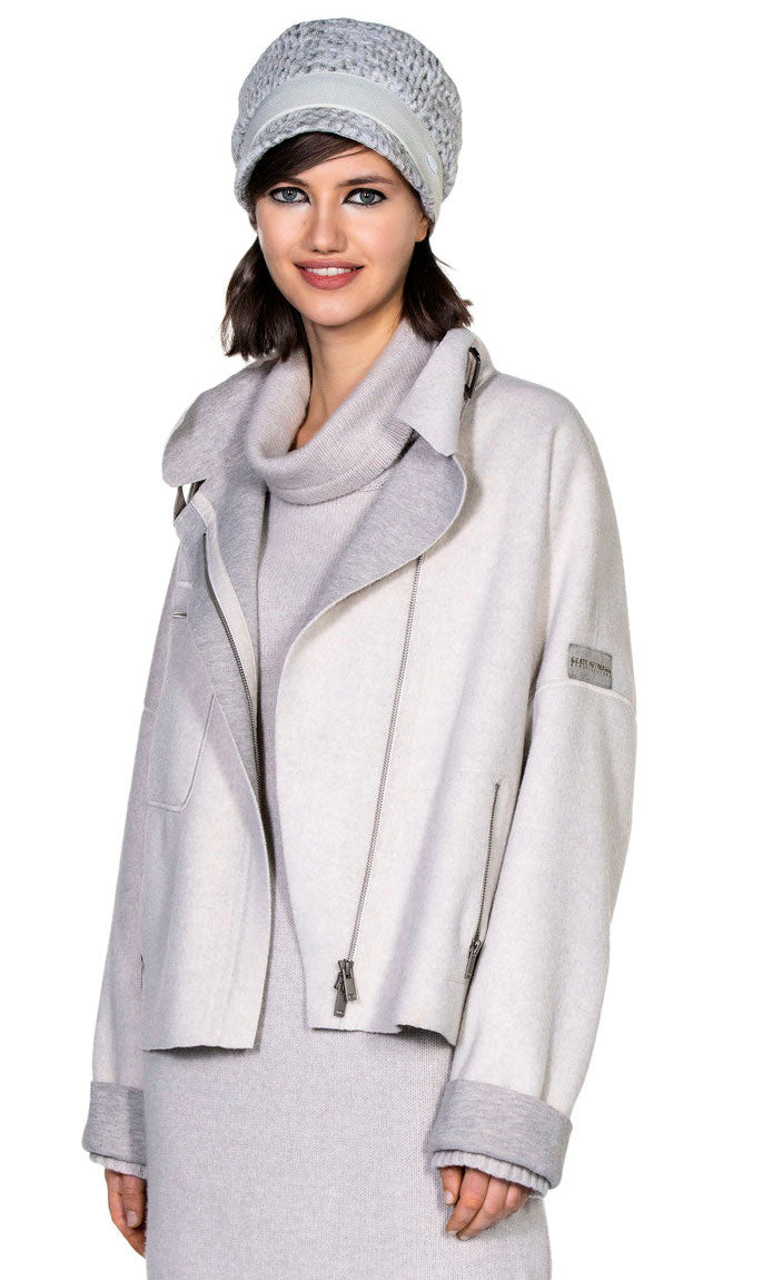 Front top half view of a woman wearing a long sweater and the beate heymann felty jacket in the color sand. This jacket is off-white with a grey lining that shows on the collar and cuffs. The jacket had drop shoulder cuffed long sleeves, an off center zipper front, a stand collar, and a front zip pocket.