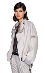 Load image into Gallery viewer, Front top half view of a woman wearing the beate heymann felty jacket in the color sand. This jacket is off-white with a grey lining that shows on the collar and cuffs. The jacket had drop shoulder cuffed long sleeves, an off center zipper front, a stand collar, and a front zip pocket.
