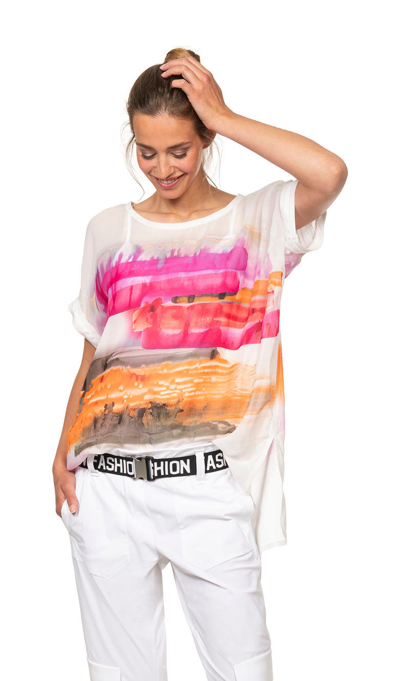 front top halfview of a woman wearing the beate heymann sunset painting top. This top is white with a painted abstract sunset print on the front. It has short sleeves, a high-low hem, and side slits.