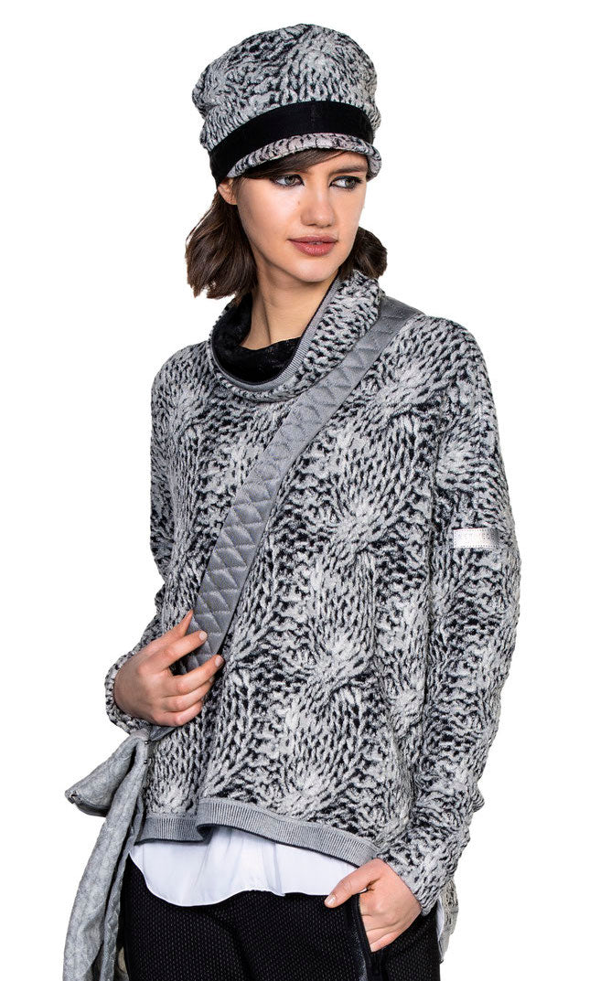 Front top half view of a woman wearing the beate heymann chunky knit pullover. This top has long sleeves, a mock neck with black lining, and a grey, loose knit appearance.